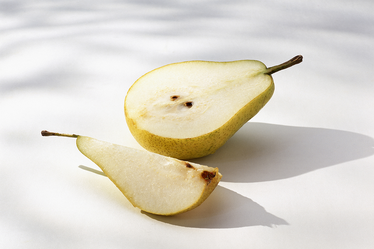A ripe yellow pear sliced in half, with one half lying flat and the other piece, a quarter segment, resting in front on a white surface with soft shadows.