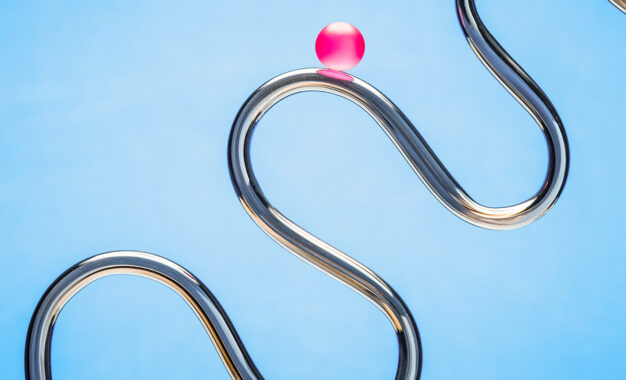 A shiny, metallic, winding track forms curves against a blue background, with a single pink ball balanced on one of the upper bends.