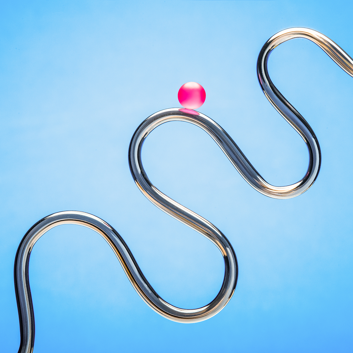 A shiny, metallic, winding track forms curves against a blue background, with a single pink ball balanced on one of the upper bends.