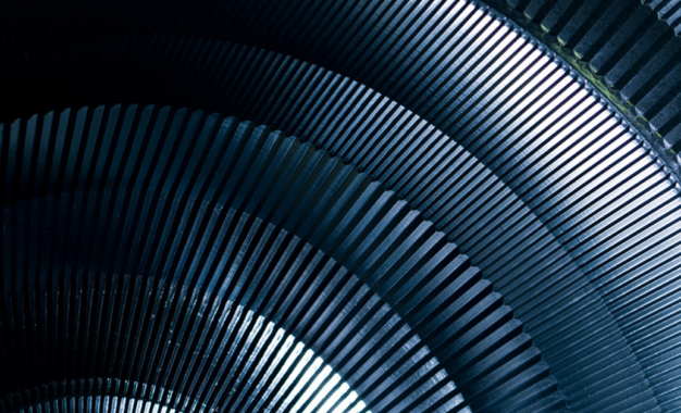 Close-up of dark metallic, ribbed, semicircular structures layered in a radial pattern, creating a repeating geometric and industrial texture with dramatic lighting and shadows.