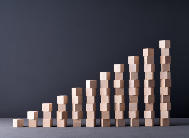 Several stacks of wooden blocks form a bar graph shape, with heights increasing from left to right, set against a plain dark background.