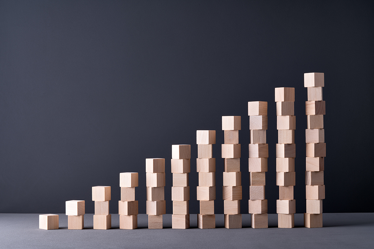 Several stacks of wooden blocks form a bar graph shape, with heights increasing from left to right, set against a plain dark background.