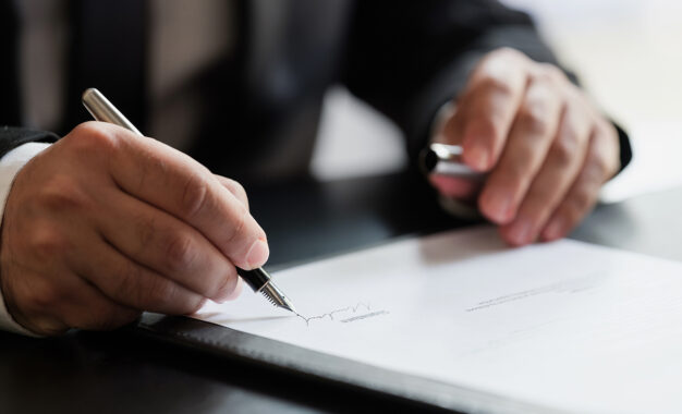 A person in a suit signing a document with a fountain pen.