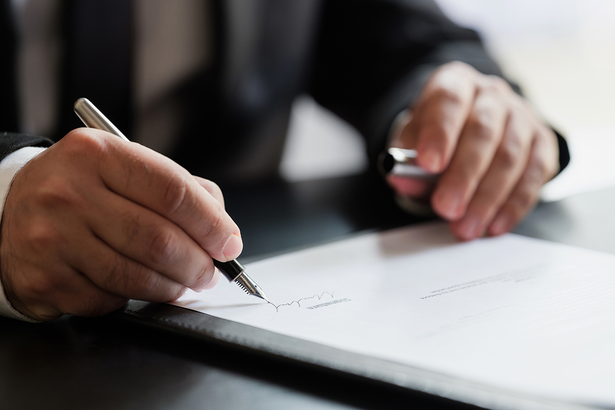 A person in a suit signing a document with a fountain pen.