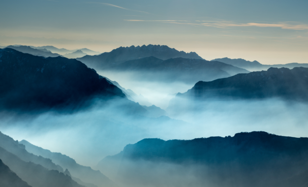 Layered mountain ranges fading into thick, blue-toned morning mist.