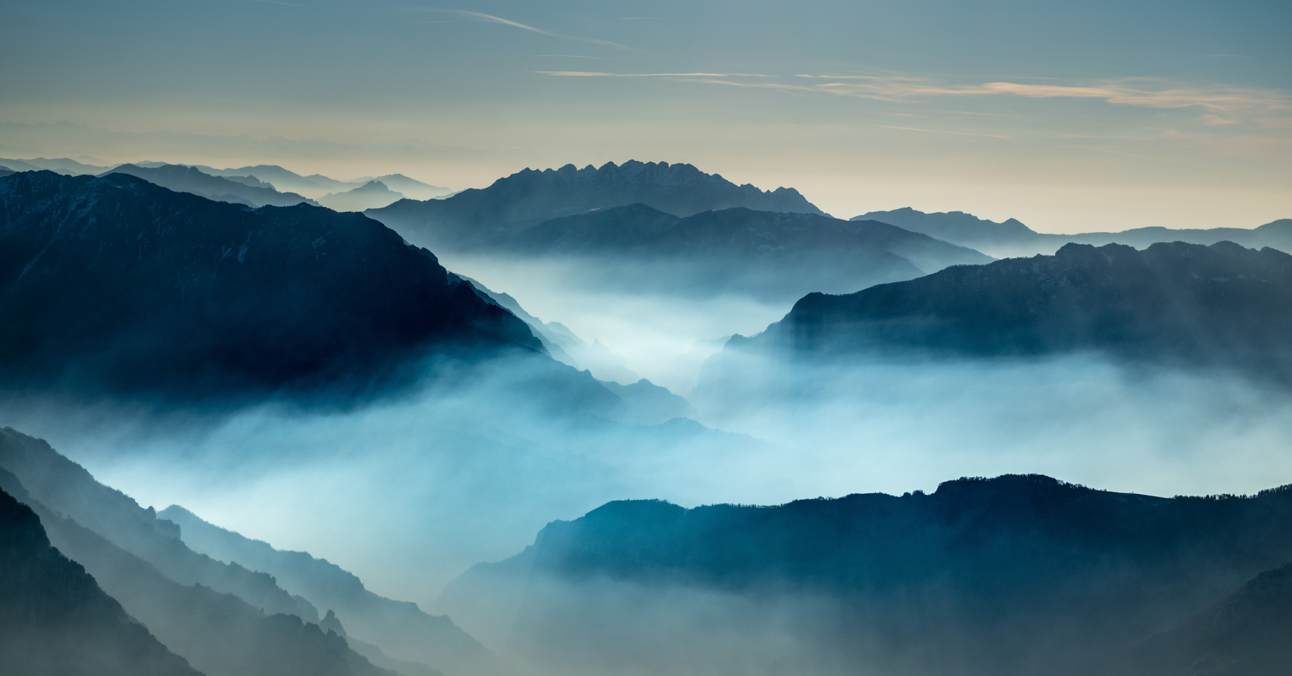 Layered mountain ranges fading into thick, blue-toned morning mist.
